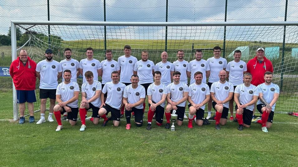 Mannschaftsfoto einer Fu&szlig;ballmannschaft in wei&szlig;en Trikots vor einem Tor auf einem Rasenplatz.