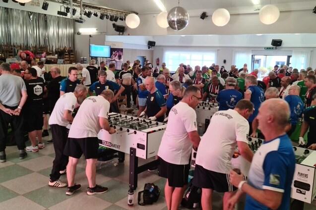Volles Turnier mit zahlreichen Teilnehmern, die an mehreren Tischkickern in einem gro&szlig;en Saal spielen.