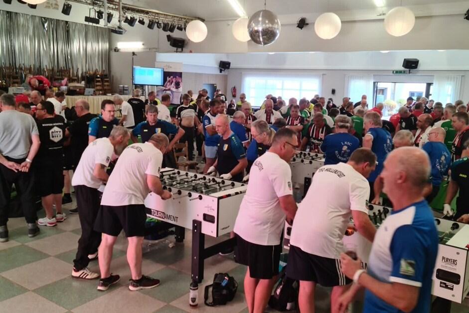 Volles Turnier mit zahlreichen Teilnehmern, die an mehreren Tischkickern in einem gro&szlig;en Saal spielen.