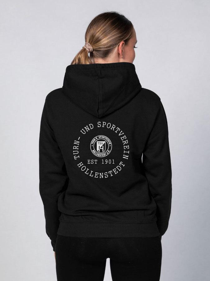 R&uuml;ckansicht einer Person in schwarzer Kapuzenjacke mit Aufdruck &bdquo;TSV Hollenstedt, Est 1901&ldquo;.