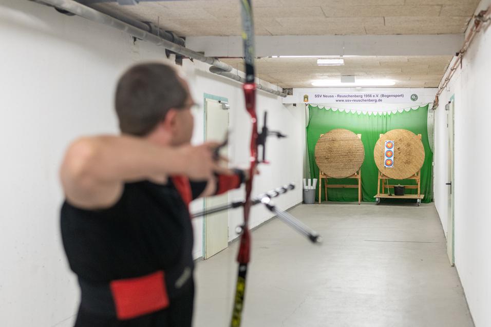 Sportler mit einem Bogen zielt auf zwei Zielscheiben in einer beschusssicheren Bogensporthalle.