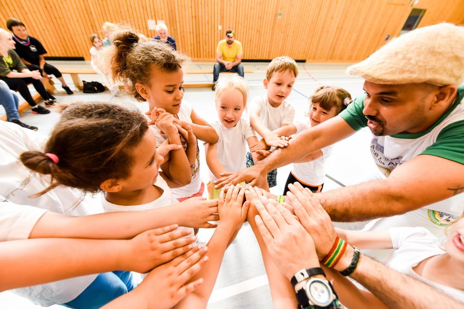 Gruppenspiel mit Kindern, die ihre Hände zum gemeinsamen Aufeinandertreffen heben, unter Anleitung eines Erwachsenen.